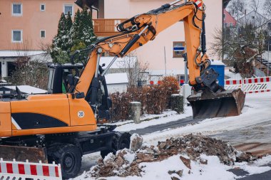 Bir inşaat kazıcısı kış tamiri sırasında yerleşim yerlerinin yakınlarındaki toprak ve enkazı temizliyor, karlı arazide çalışıyor..