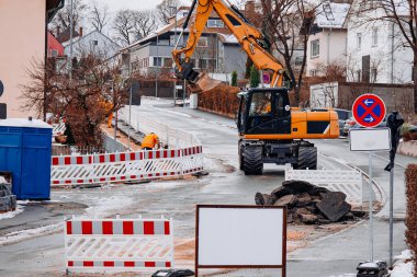 Kış yolu inşaatında çalışan bir kazıcı, karlı bir caddedeki altyapı onarım projesi sırasında paketlenmiş toprak ve enkazı kaldırıyor..