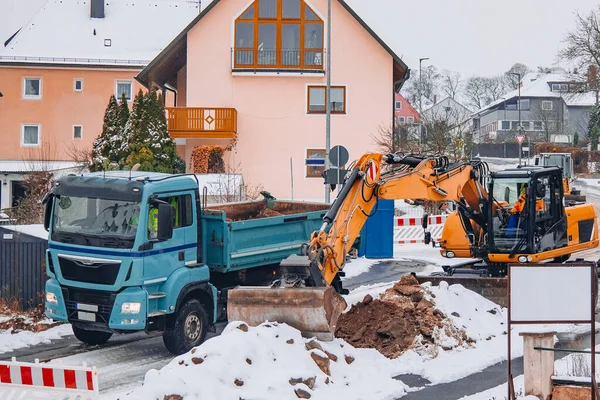 Karlı bir inşaat sahasında bekleyen bir çöp kamyonuna toprak döken kazıcı kolunun yakın görüntüsü yol bakımı sırasında.