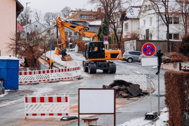Güvenlik çitleri ve karla kaplı çevresiyle çevrili bir kış yolu onarım operasyonu sırasında hasarlı asfalt parçalarını kaldıran ve kaldıran bir kazıcı..