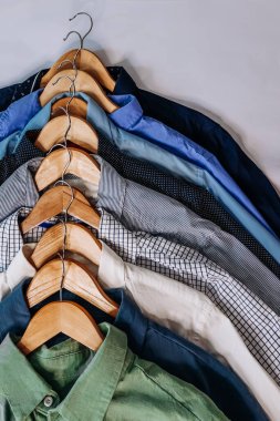 Dolabın içindeki ahşap askılarda çeşitli tonlarda mavi, gri ve beyaz erkek gömlekleri asılıydı..