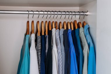 Ahşap askılarda asılı mavi, gri ve deniz mavisi gömlekli parlak, temiz bir gardırop..