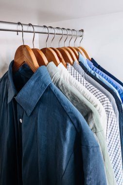 Bir ev gardırobundaki ahşap askılarda asılı mavi ve nötr renkli gömleklerden oluşan bir kolleksiyon..