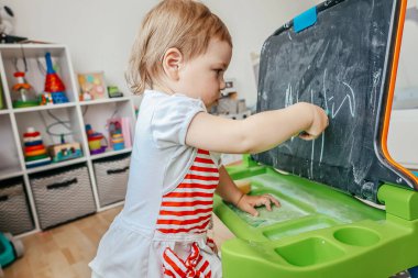 Evdeki küçük kız oyun oynuyor ve küçük bir tahtaya resim çiziyor. Erken çocukluk eğitimi, yaratıcılık gelişimi, oyun yoluyla öğrenme ve konforlu bir ev ortamında Montessori 'den esinlenilmiş faaliyetler.