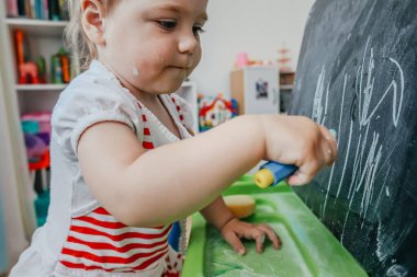 Evde oyun saatinde küçük bir tahtaya tebeşirle tebeşirle tuhaf bebek çizimi. Erken çocukluk eğitimi, yaratıcılık, oyun konseptiyle öğrenme.