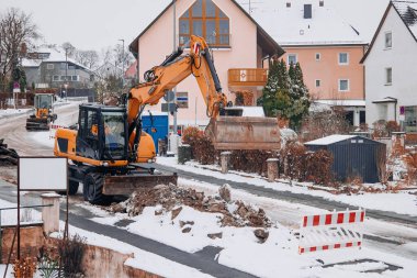 Kazı sırasında kazıcı kazıyor ve toprağı temizliyor. Kışın bir şehir caddesinde çalışıyor. Altyapı iyileştirme, kentsel kalkınma ve inşaat endüstrisi kavramı.