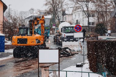 Sarı kazıcı, kış aylarında karlı bir sokakta park levhası ve güvenlik bariyeri olmayan bir kamyonun yanında çalışıyor..