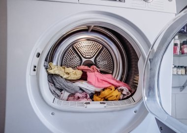 Açık bir çamaşır kurutma makinesinin içinde renkli giysiler yığını. Ev çamaşırları, ev işleri, kumaş kurutma ve günlük rutin konsept..