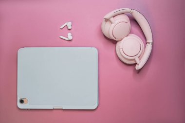 Pastel arka planda çok az tablet ve pembe kulaklık, modern teknoloji ve çalışma alanı kavramı