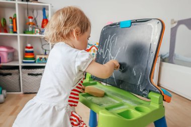 Evdeki tahtaya tebeşirle çizen küçük kız.