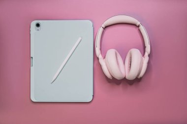 Stylus 'lu düz tablet ve pembe arka planda kablosuz kulaklık. Kopyalama alanı olan asgari teknoloji çalışma alanı.