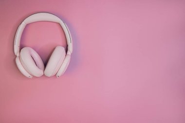 Pastel pembe arka planda, kulaklıklar üzerinde en az pembe kablosuz televizyon yayını. Modern ses aygıtı kavramı.