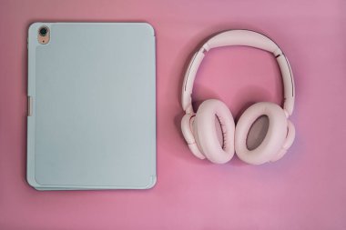 Tabletli ve kulaklıklardan kulaklıklı, pastel pembe arka planda minimum düz yatıyordu. Dijital yaşam tarzı kavramı.