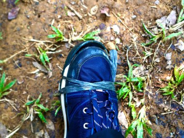 Çok yıpranmış bir ayakkabıyı doğaçlama bir çözüm olarak basit bir plastik şeritle bağlayan makro bir çekim. Topraksı arka plan ve detaylı dokular dayanıklılığı ve minimalizmi vurgular