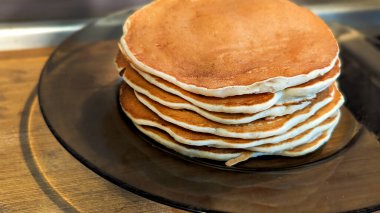 Büyük bir yığın ev yapımı krep. Koyu bir tabakta, ahşap bir masanın üzerinde. Kahverengi dokular sergileniyor.