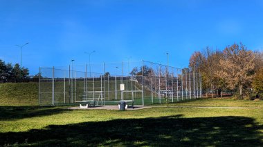 Huzurlu bir şehir parkında yeşil çimenler, ağaçlar ve açık mavi gökyüzüyle çevrili modern bir futbol sahası. Spor, eğlence ve eğlence için mükemmel bir açık hava alanı.