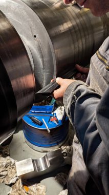 Profesyonel bir teknisyen, bir ticari gemi atölyesinde özel bakım ve onarım çalışmaları sırasında büyük bir çelik motor krank mili üzerinde hassas bir ölçüm aracı kullanır.