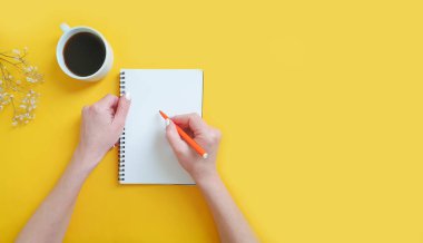 Bir fincan kahve tutan kadın elleri, renkli bir arka planda not defteri.