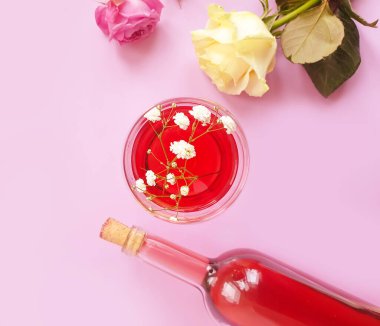 Bir şişe şarap, renkli arka planda bir bardak çiçek gülü.