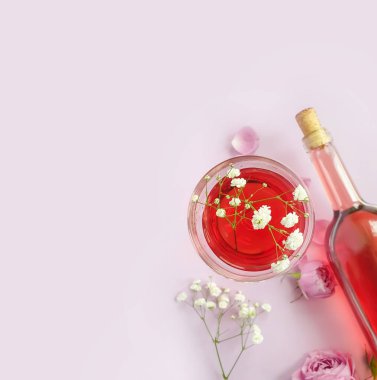 Bir şişe şarap, renkli arka planda bir bardak çiçek gülü.