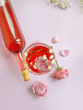 Bir şişe şarap, renkli arka planda bir bardak çiçek gülü.