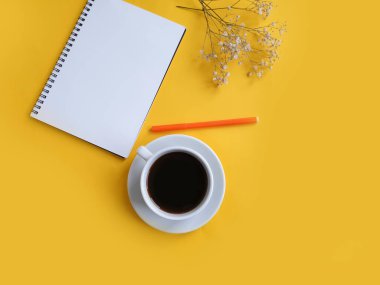 Kahve fincanı, not defteri, renkli arka planda çiçek.