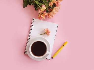Bir fincan kahve, bir defter, renkli arka planda bir çiçek.