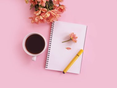 Bir fincan kahve, bir defter, renkli arka planda bir çiçek.