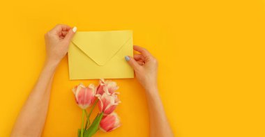 Kadın eli bir zarf tutar, bir buket lale.