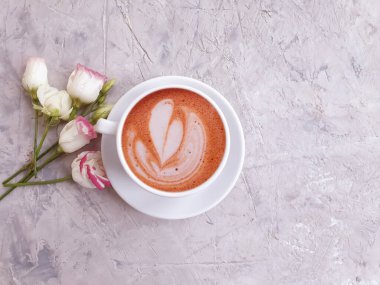 Bir fincan kahve, arka planda gül çiçeği.