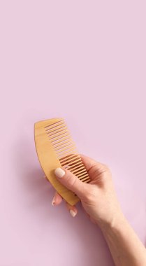 Kadın eli, arka planda ahşap bir tarak tutuyor.