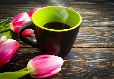 Bir fincan kahve, ahşap arka planda lale.