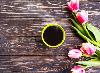 Bir fincan kahve, ahşap arka planda çiçek lalesi.