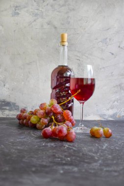 Kırmızı şarap kadehi, beton zeminde taze üzümler.
