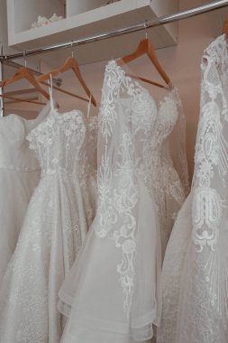 Gelinlik mağazasında şık gelinlikler sergileniyor. Her elbisede karmaşık dantel desenler ve yumuşak kumaşlar var. Müstakbel gelinler için mükemmel bir romantik ortam yaratıyor..