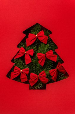 Christmas tree cutout filled with green branches and red bows on red background.