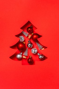 Parlak kırmızı arka planda gümüş süslemelerle dolu bir Noel ağacı..