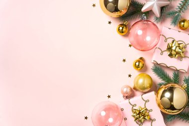 Pembe ve altın rengi Noel süsleri yumuşak bir pastel arka planda dizilmiş..