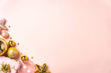 Pembe ve altın rengi Noel süsleri yumuşak bir pastel arka planda dizilmiş..