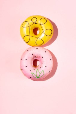 Yumuşak pembe arka planda dikey dizilmiş iki renkli donut..
