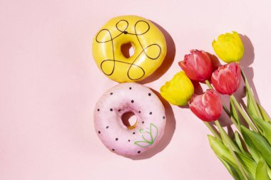 Yumuşak pembe arka planda dikey dizilmiş iki renkli donut..