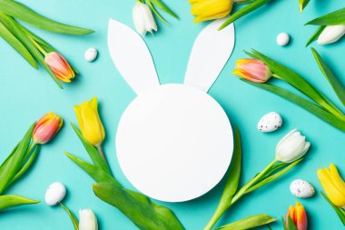 Paskalya tavşanı şekli. Etrafı bahar laleleri ve turkuaz arka planda yumurtalarla çevrili..