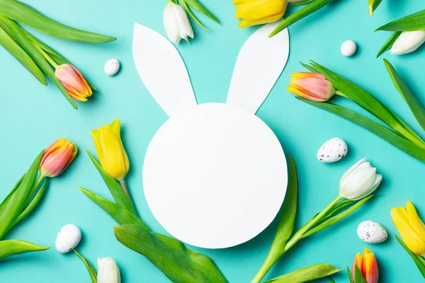 Paskalya tavşanı şekli. Etrafı bahar laleleri ve turkuaz arka planda yumurtalarla çevrili..