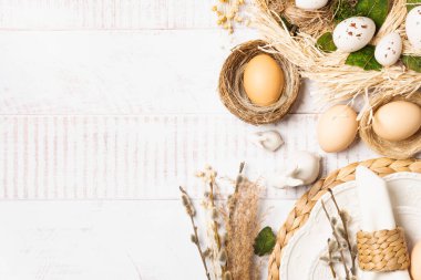 Yuvada yumurtalar, beyaz ahşap bir masa üzerinde buğday ve bahar çiçekleri olan Paskalya arkaplanı. Kopya alanı olan bayram kompozisyonu..