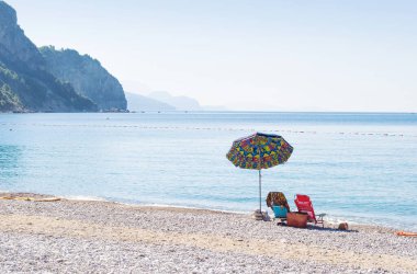 Budva yakınlarındaki Jaz sahilindeki bir körfezde, bir renkli şemsiye altında kayalık tepelere karşı iki sandalye, sakin mavi deniz. Mavi bulutsuz sabah gökyüzü. Karadağ ve Akdeniz