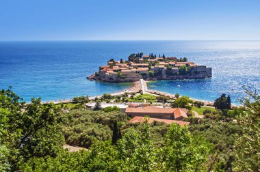 Eski Sveti Stefan Yarımadası 'nın kırmızı çatıları ve taş duvarları ılık bir yaz sabahı sisli mavi dalgalı deniz suyuna karşı. Karadağ. Yüksek açı görünümü