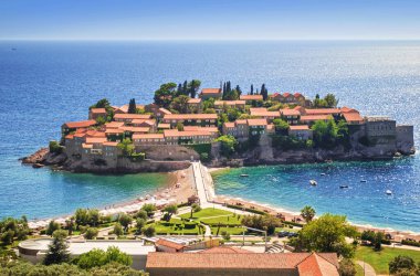 Eski Sveti Stefan Yarımadası 'nın kırmızı çatıları ve taş duvarları ılık bir yaz sabahı sisli mavi dalgalı deniz suyuna karşı. Karadağ. Yüksek açı görünümü