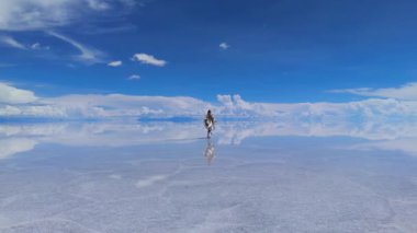 Bir kadın, Bolivya 'daki geniş Salar de Uyuni tuz düzlüklerinde yürür. Yansıması sığ suda mükemmel bir şekilde aynalıdır..