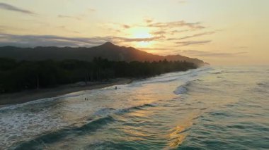 Günbatımında sakin bir Kolombiya plajının hava görüntüsü, Yoğun Orman ve Görkemli Dağlar.