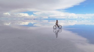 Bolivya 'daki geniş Salar de Uyuni tuz düzlüklerinde bisiklet süren bir kadın yansıyan gökyüzünün gerçeküstü güzelliğini yakalıyor..